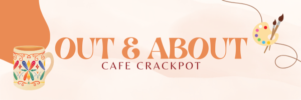 A colorful banner with the title 'Out & About' in large orange typography, followed by 'Café Crackpot' in smaller red text underneath. On the left side, there's an illustrated mug with vibrant, abstract designs, and on the right side, a painter’s palette with colorful paint blobs and brushes. The background features soft beige and orange tones, with a flowing line adding a decorative touch